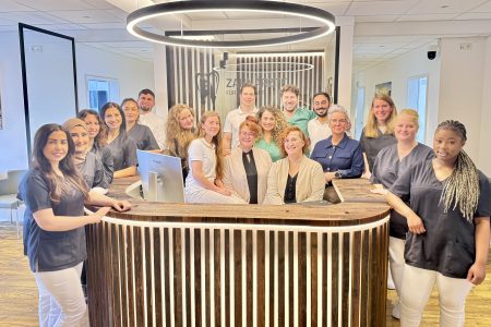 Das Team der Zahnarztpraxis Zahnärzte für Erftstadt steht gemeinsam an der Rezeption. Moderne Praxis mit freundlichem Personal.